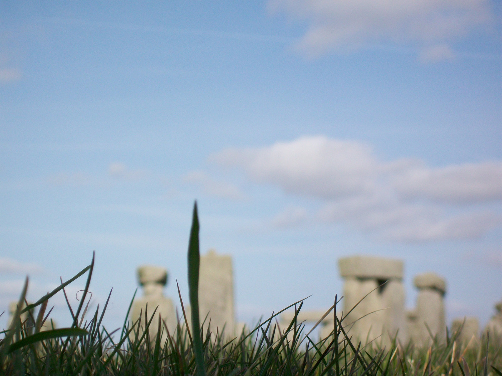 Blurred Stonehenge standing stones behind sharp blades of grass under a blue sky