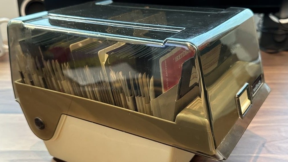 Photo of a vintage smoked-plastic storage box packed with old 5.25-inch floppy disks, sitting on a wooden desk