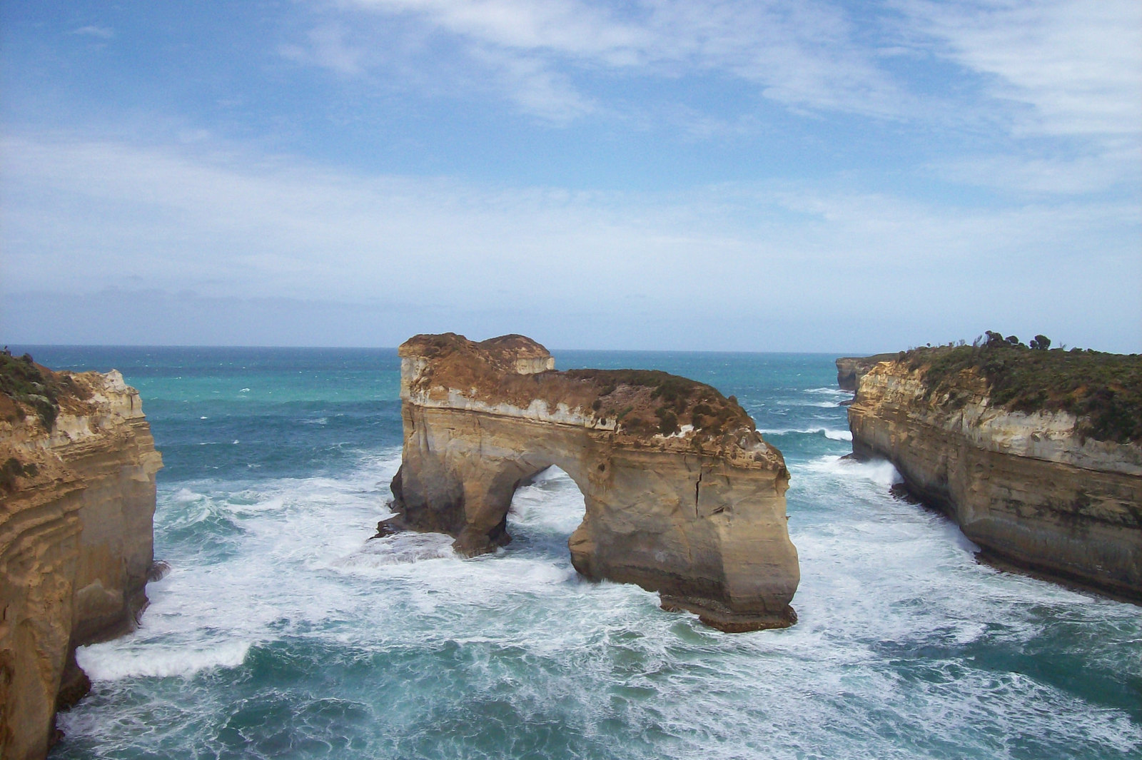 Sea arch rising from churning surf between sandstone cliffs under a cloudy sky